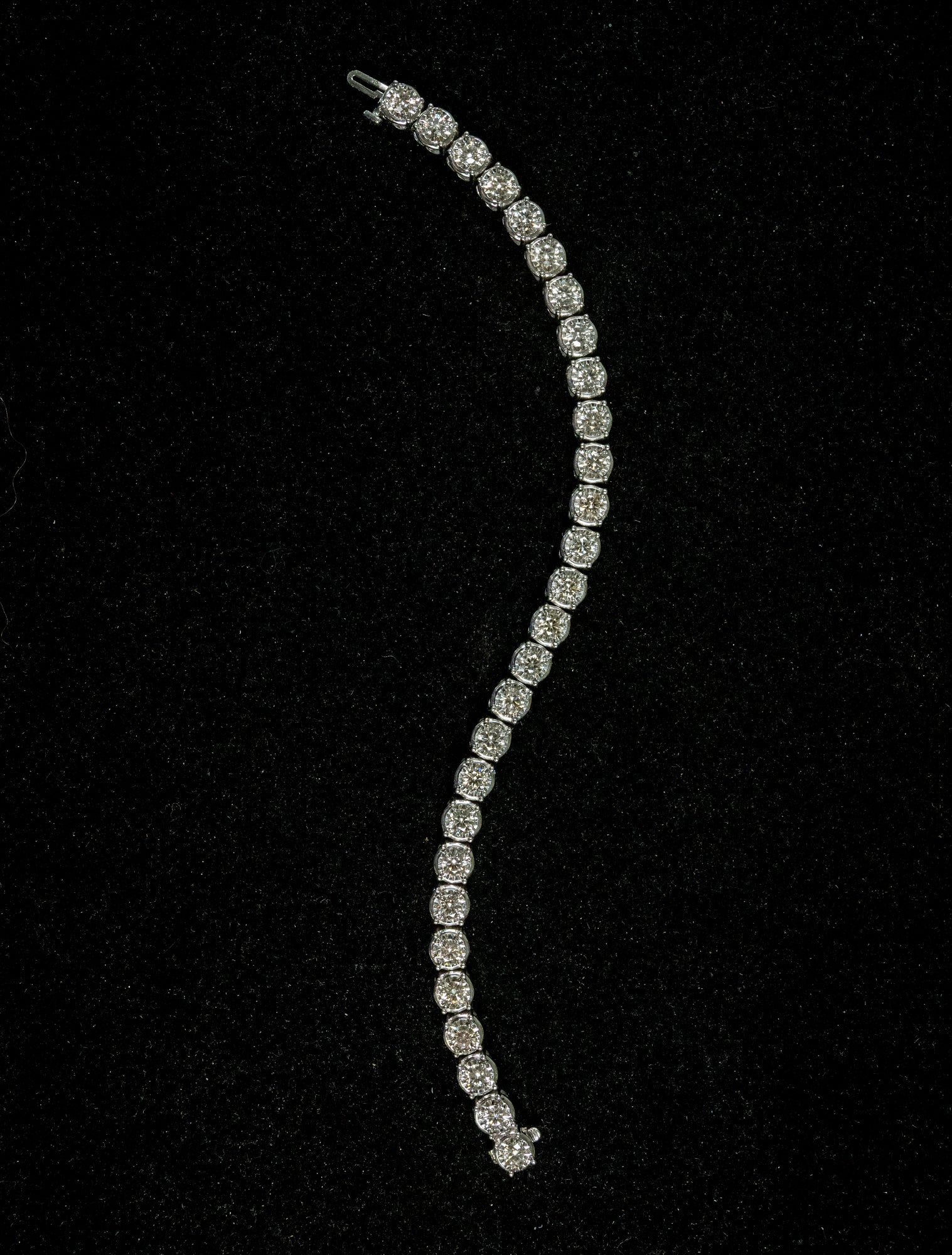 A curved white gold tennis bracelet set with diamonds, displayed on a textured black background.