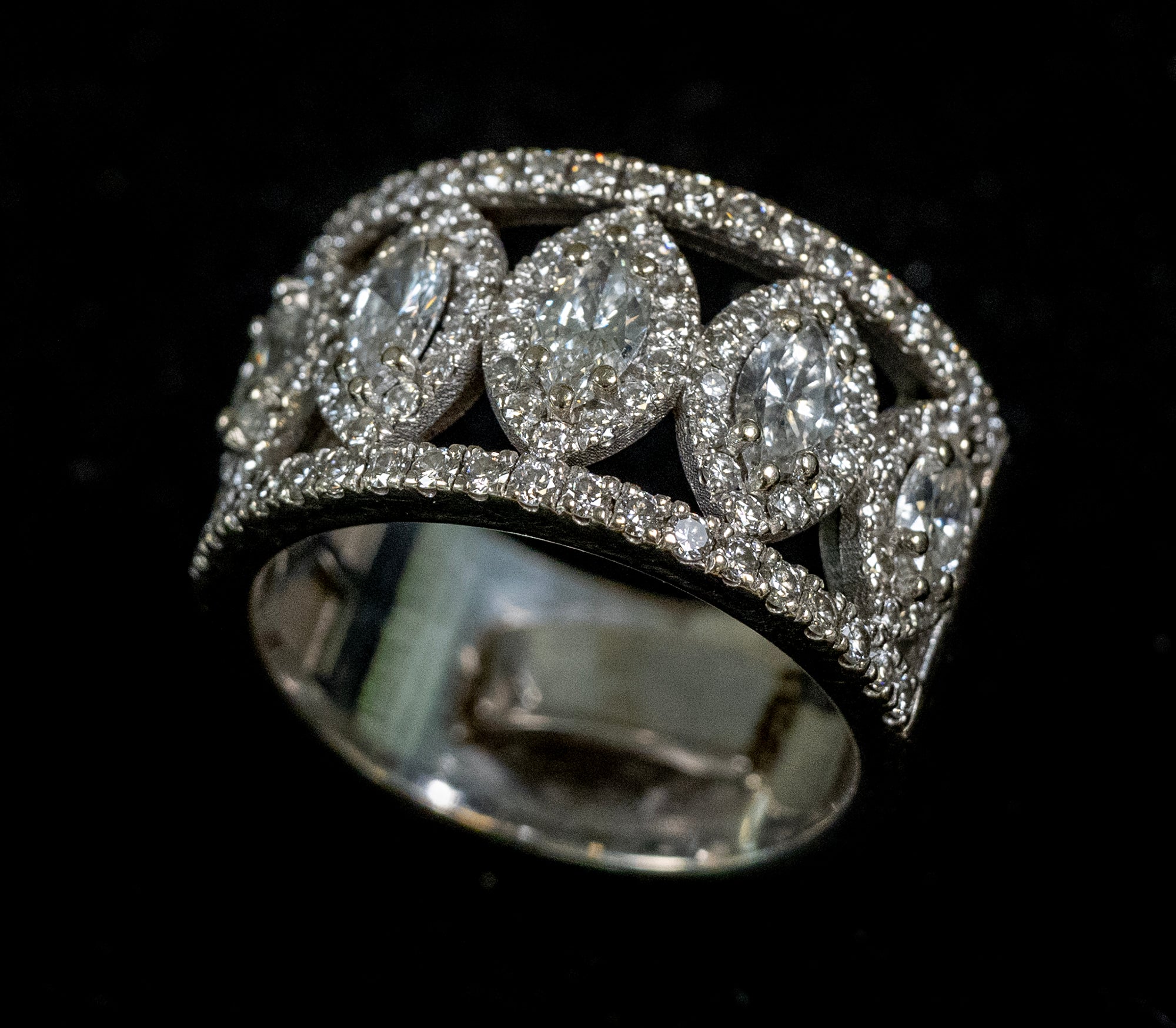A wide white gold ring set with multiple marquise and oval diamonds on a black background.