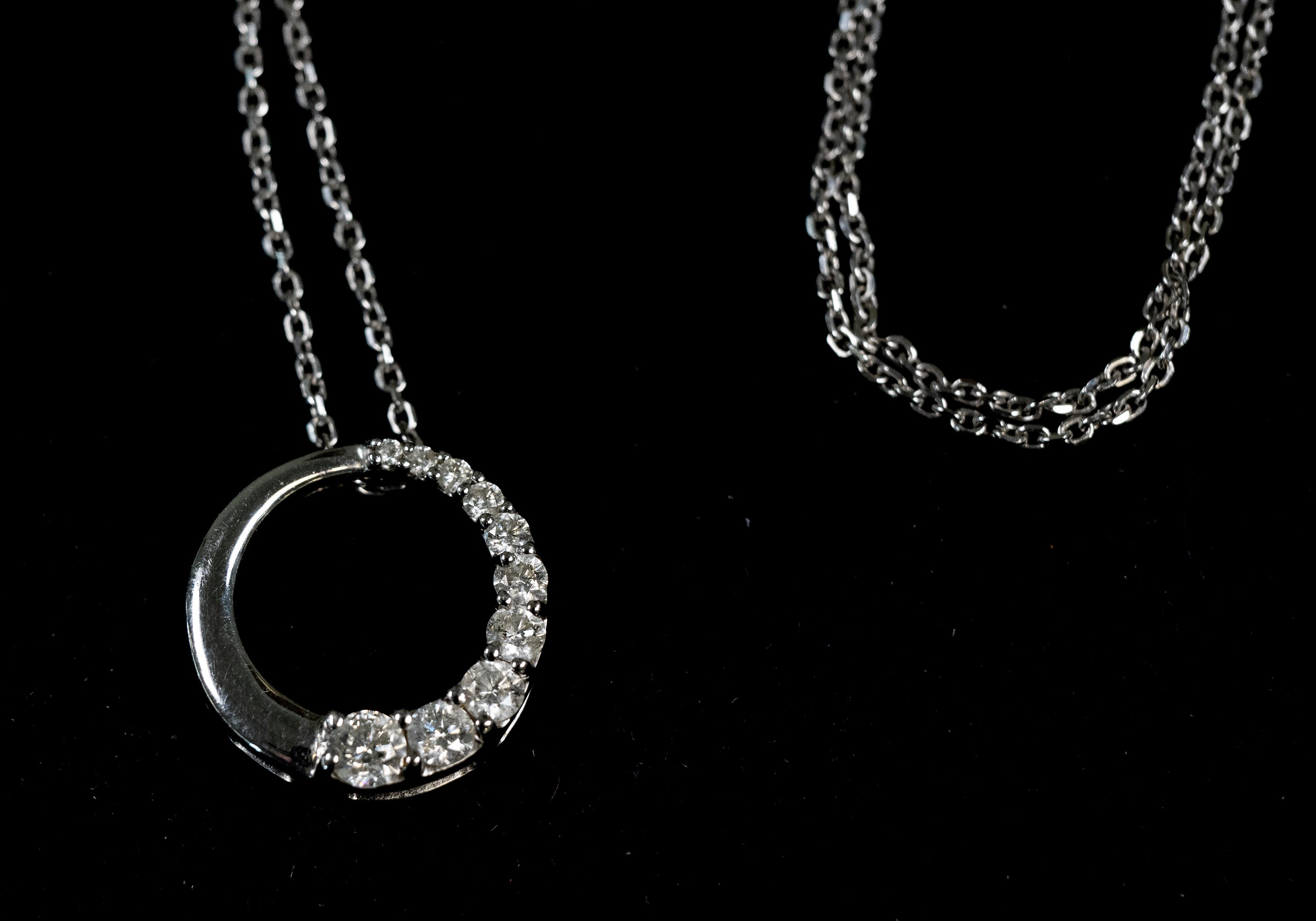 A white gold necklace with a crescent moon pendant partially encrusted with diamonds, displayed against a solid black background.