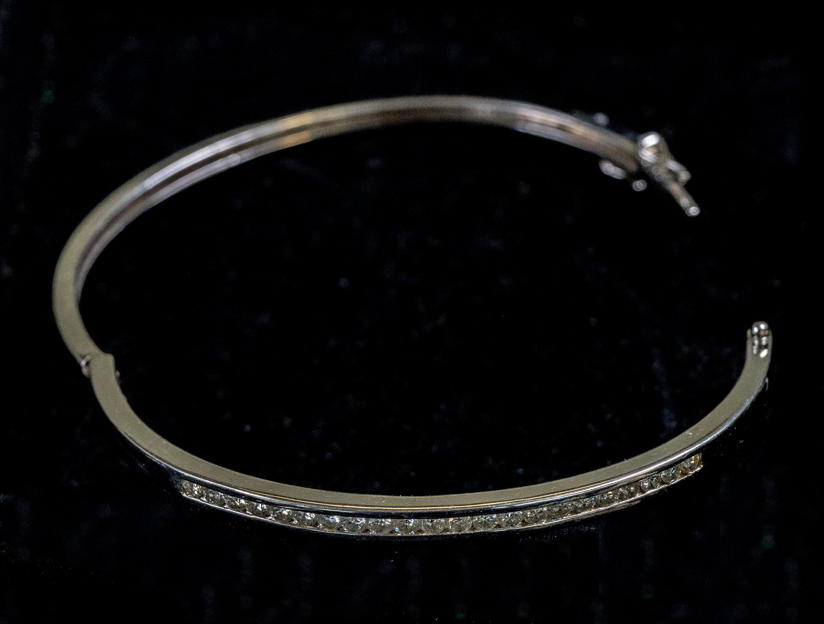 A polished silver-toned open cuff bracelet with a row of small clear stones along the front, displayed on a black velvet background.
