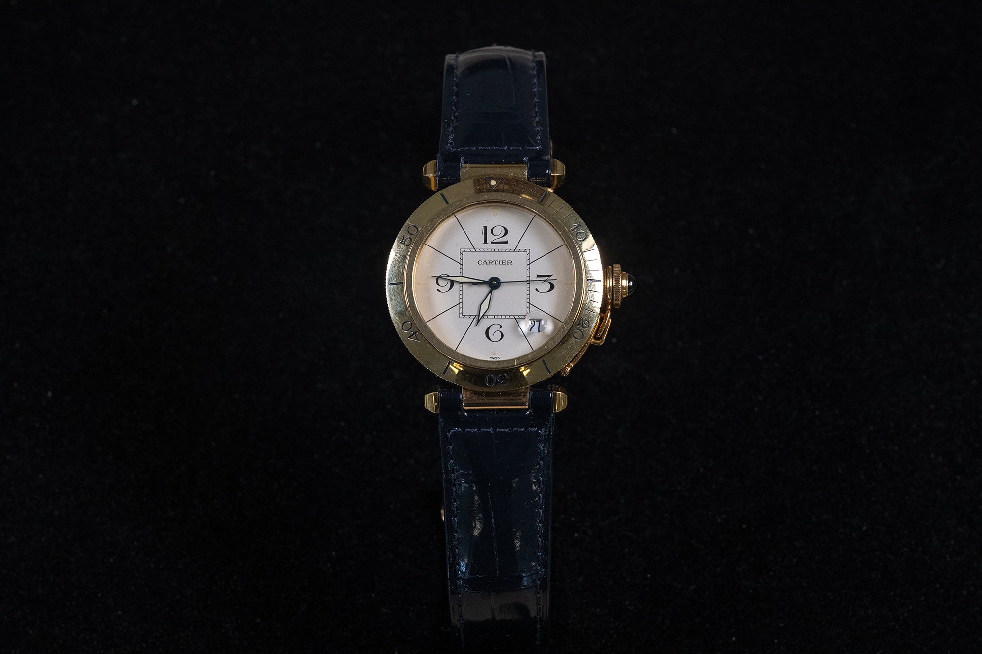 A Cartier watch with a gold-tone case, white dial, and dark blue leather strap, centered against a solid black background.