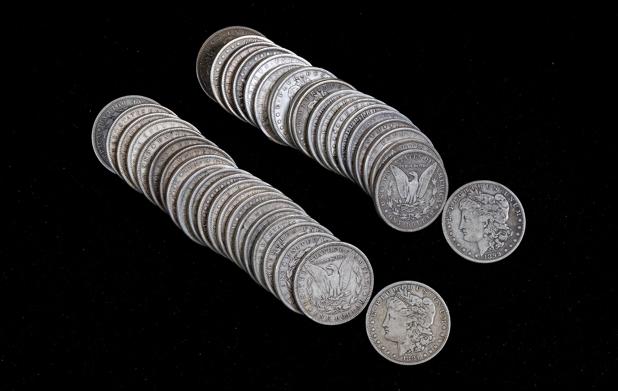 Two stacks of silver Morgan dollars with two loose coins displayed on a solid black background.